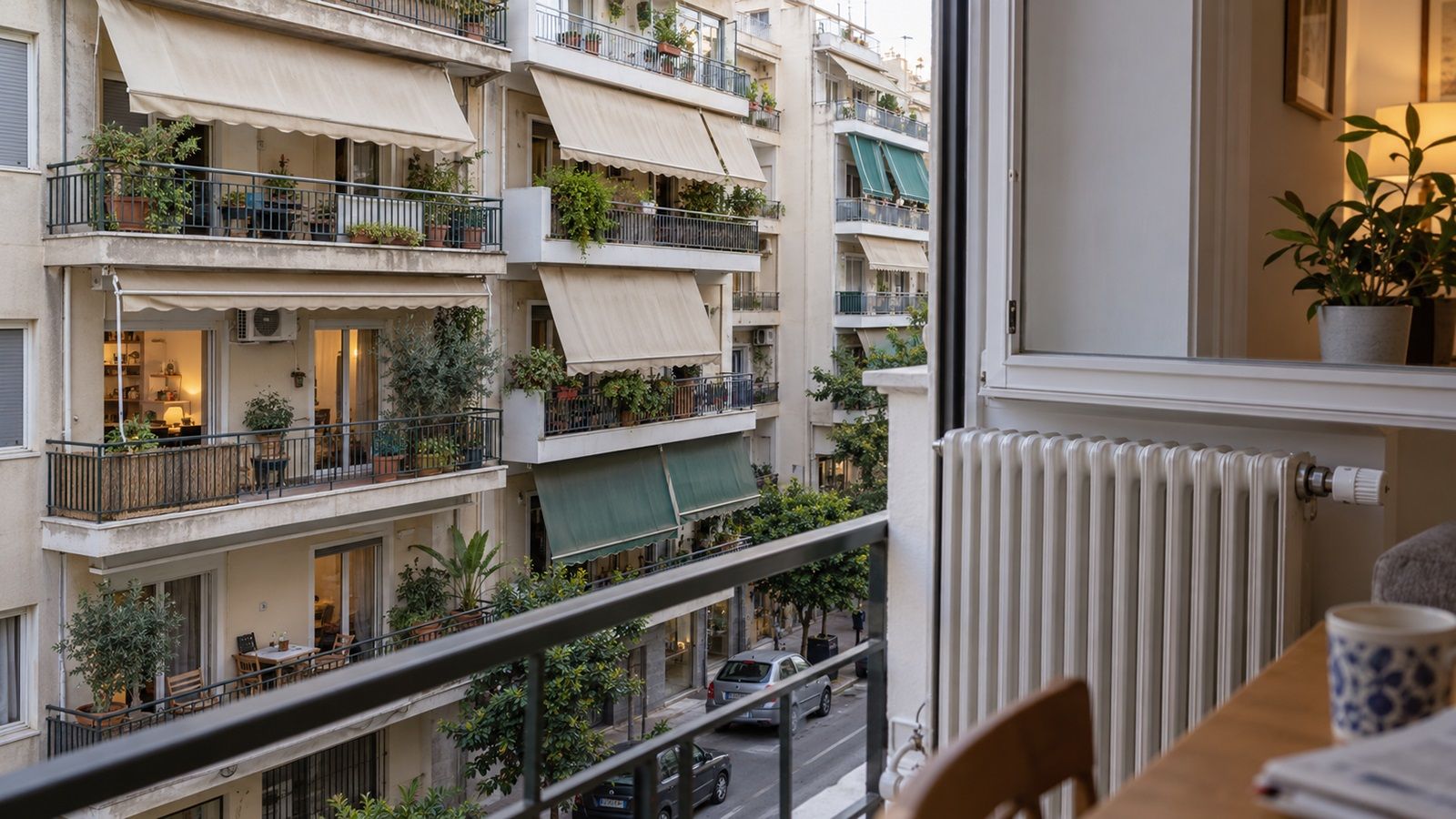 Συνηθισμένη αθηναϊκή πολυκατοικία με μπαλκόνια και τέντες, όπως φαίνεται από παράθυρο διαμερίσματος με σώμα καλοριφέρ