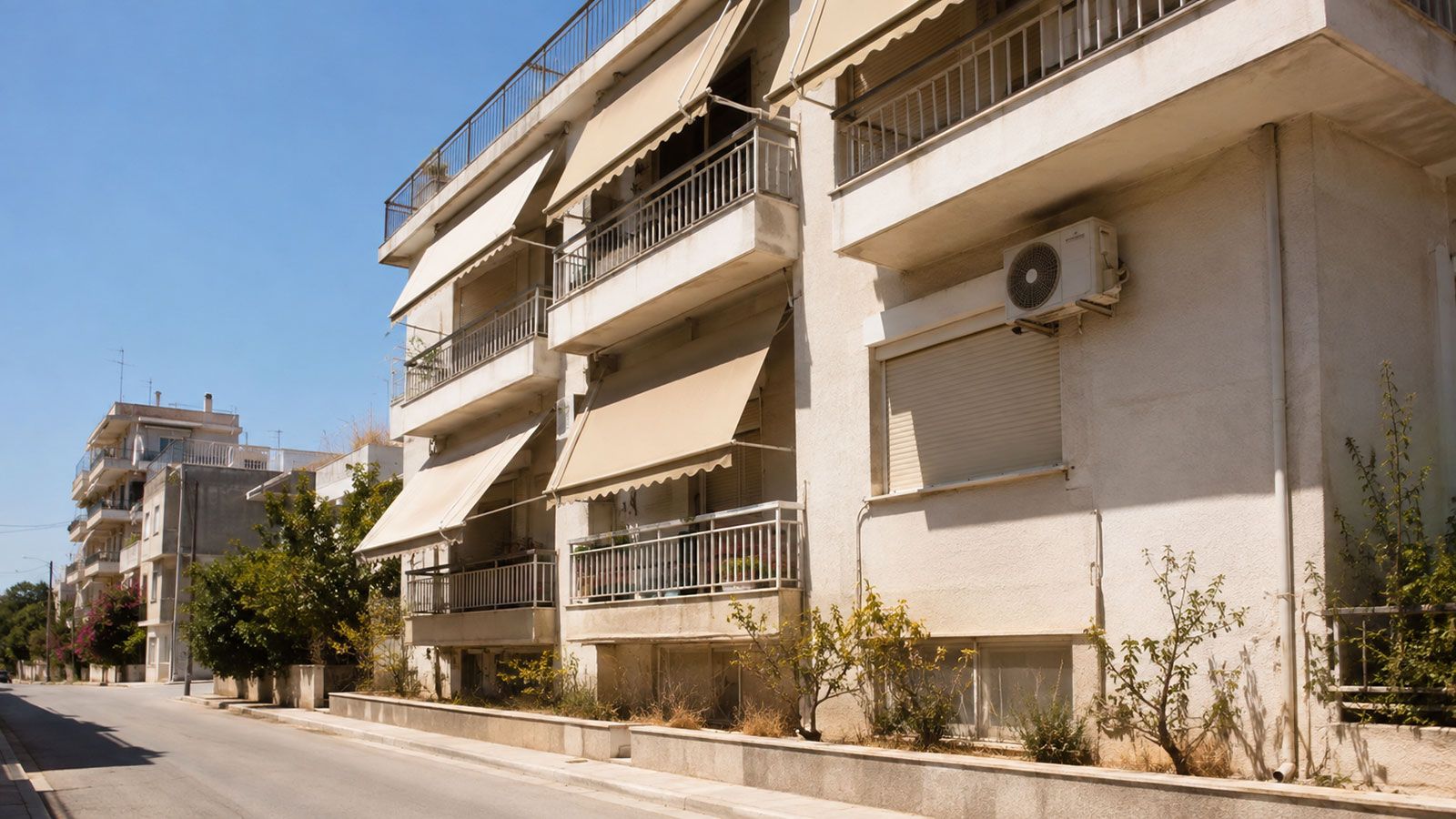 Ελληνική πολυκατοικία με τέντες και εξωτερική μονάδα κλιματιστικού κάτω από έντονο μεσημεριανό ήλιο.